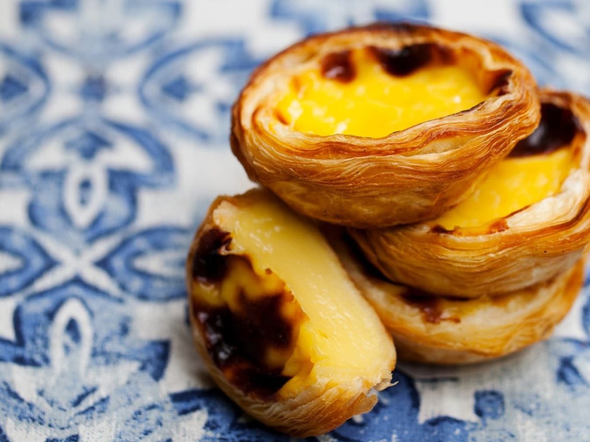 ein Stapel veganer Pasteis de Nata auf blau-weißen Fliesen.