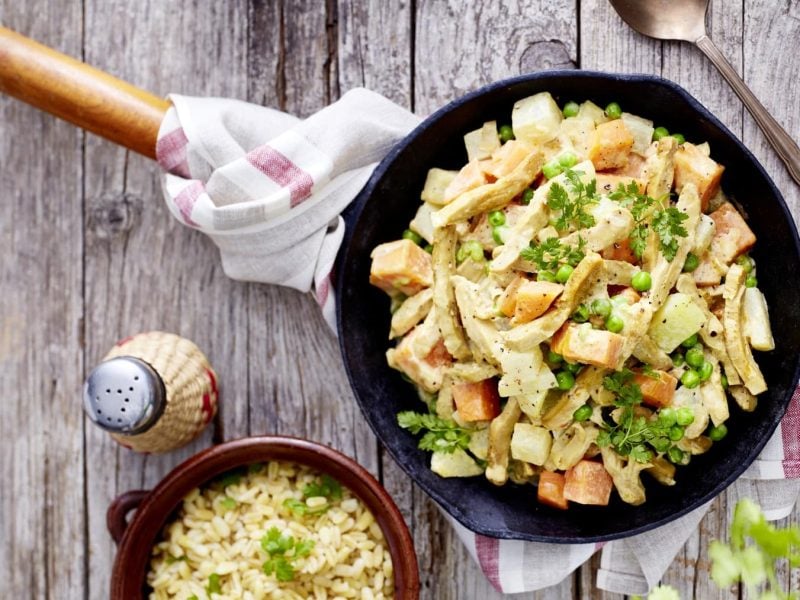 Veganes Geschnetzeltes in einer Pfanne. Daneben Besteck und weitere Zutaten.