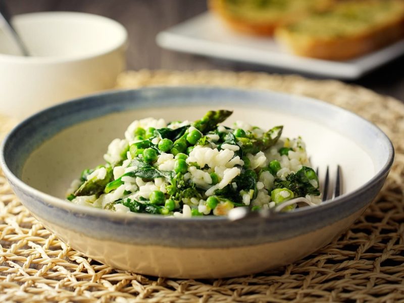 Veganes Spargelrisotto mit Spinat und Erbsen auf einem tiefen Teller mit einer Gabel.