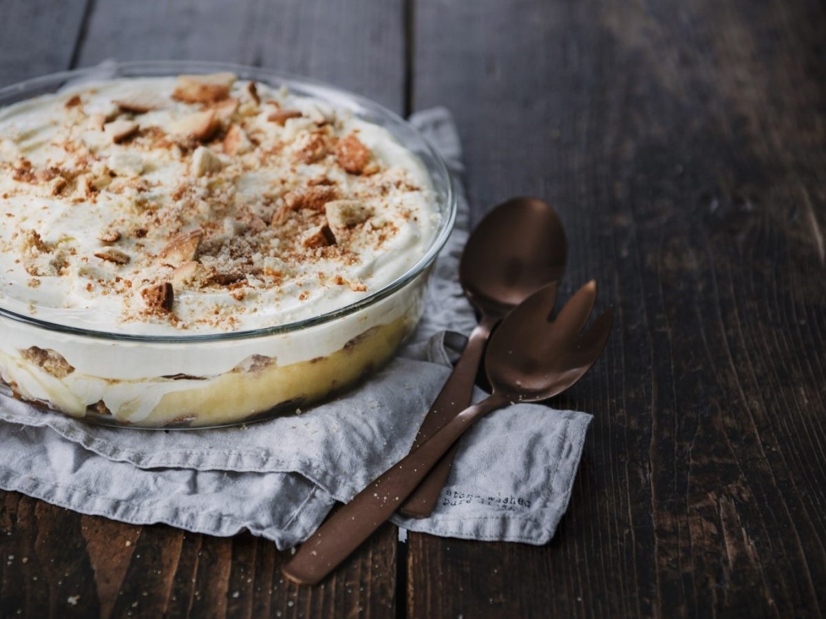 Zitronen-Quark-Trifle mit Keksen in einer durchsichtigen Auflaufform geschichtet und serviert auf einem dunklen Holztisch.