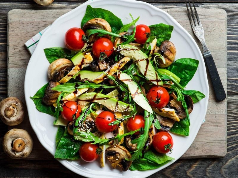 Avocado-Salat mit Pilzen und Tomaten auf weißem Teller, angerichtet auf hölzernem Untergrund