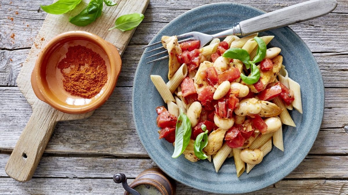 Auf einem Teller ist eine Portion Blitz-Penne angerichtet. Sie ist mit Basilikum garniert.