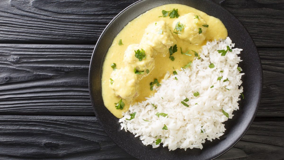 Boller i Karry – dänische Hackbällchen in Currysauce mit Reis auf dunklem Holzuntergurnd.