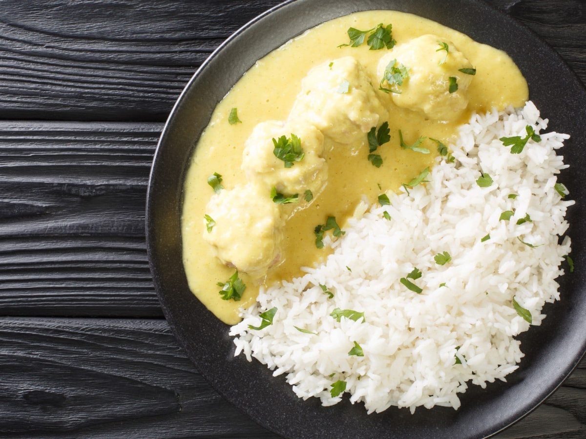 Boller i Karry – dänische Hackbällchen in Currysauce mit Reis auf dunklem Holzuntergurnd.