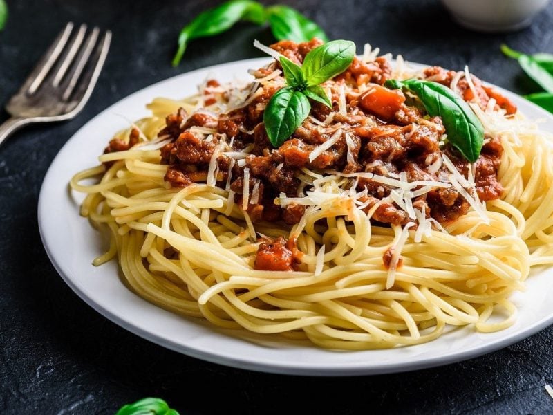 Spaghetti Bolognese bestreut mit Parmesan und Basilikum auf dunklem Untergrund