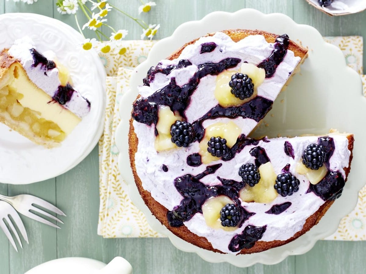 Auf einem Teller steht eine Birnen-Brombeer-Schmandtorte. Sie ist mit Brombeeren und Birnen und einer Creme bedeckt.