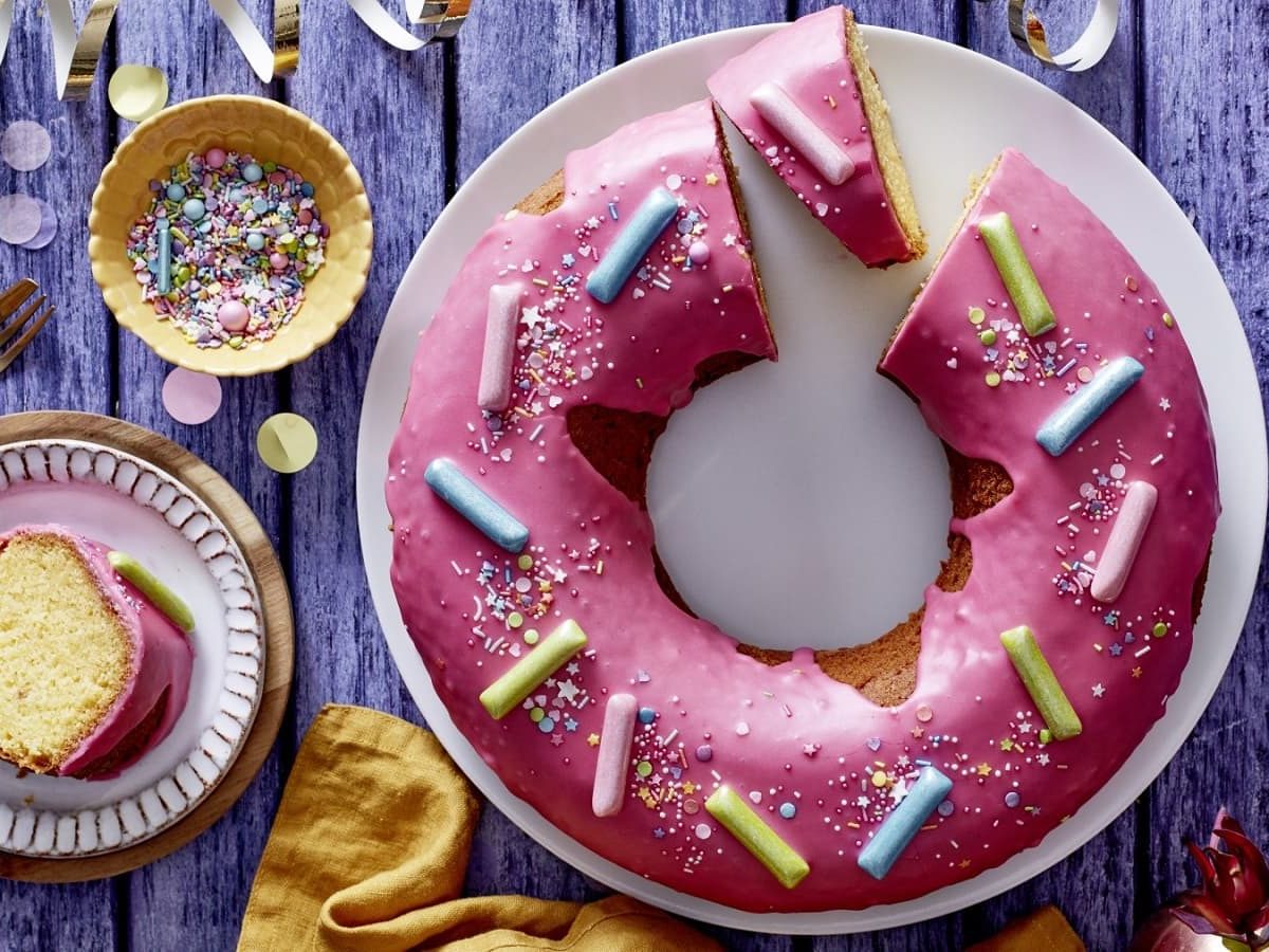 Auf einem lila Tisch steht ein Teller mit einem Donut-Kuchen. Er ist mit Streuseln und Kaubonbons verziert.