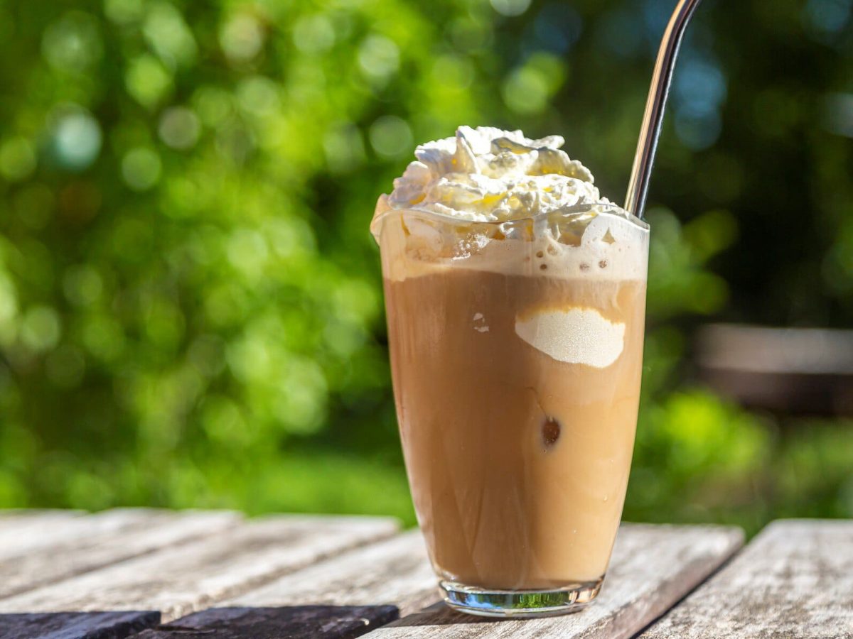 Eiskaffee mit Vanilleeis und Schlagsahne auf einem Gartentisch aus Holz.