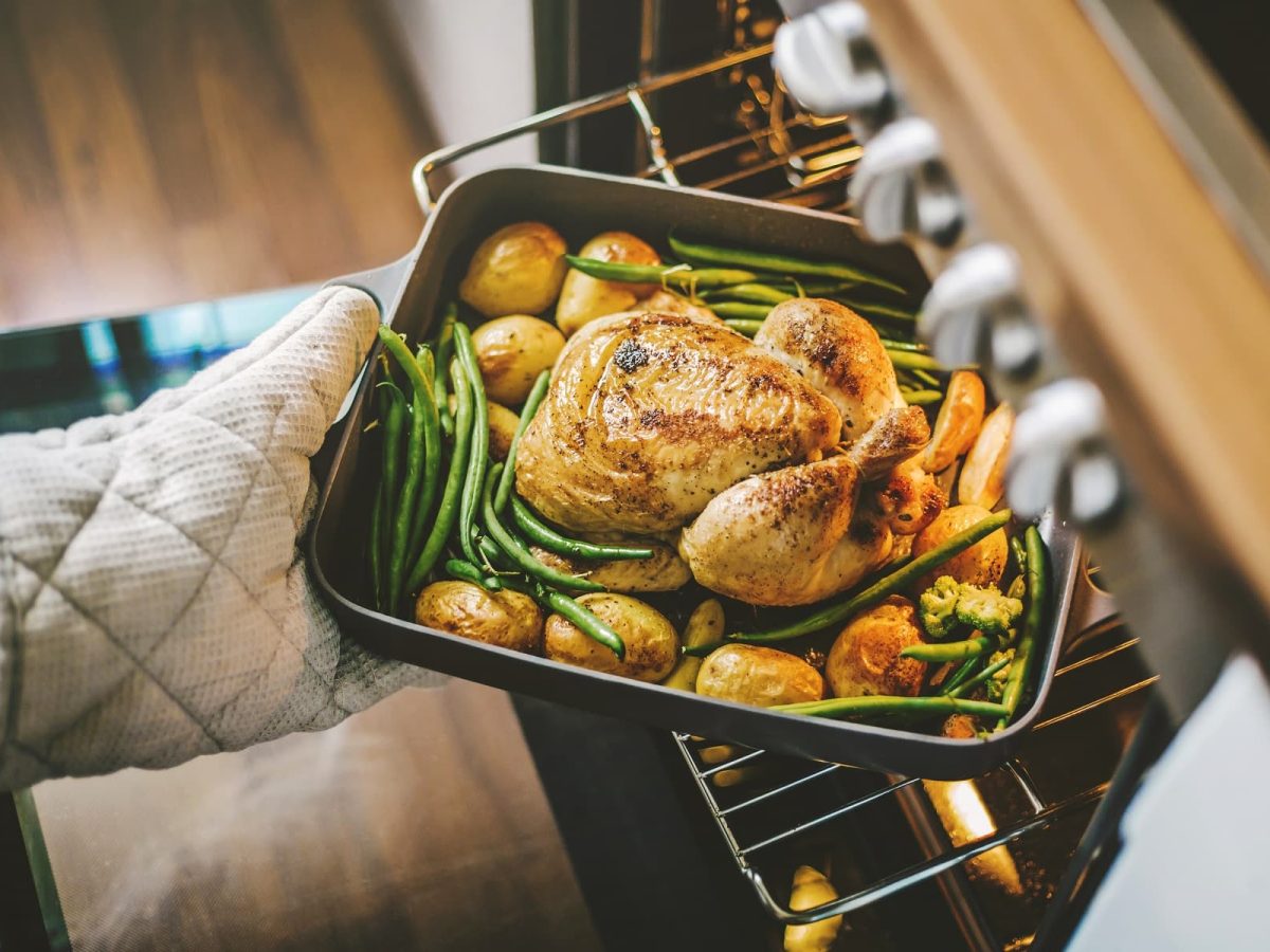 Hähnchen mit Kartoffeln und Bohnen werden in Auflaufform in den Backofen geschoben.