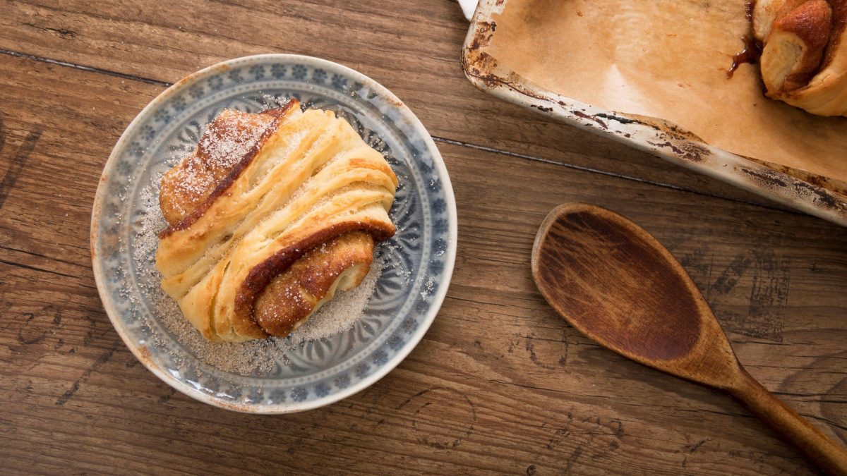 Franzbrötchen auf Teller, drapiert auf hölzernem Untergrund.