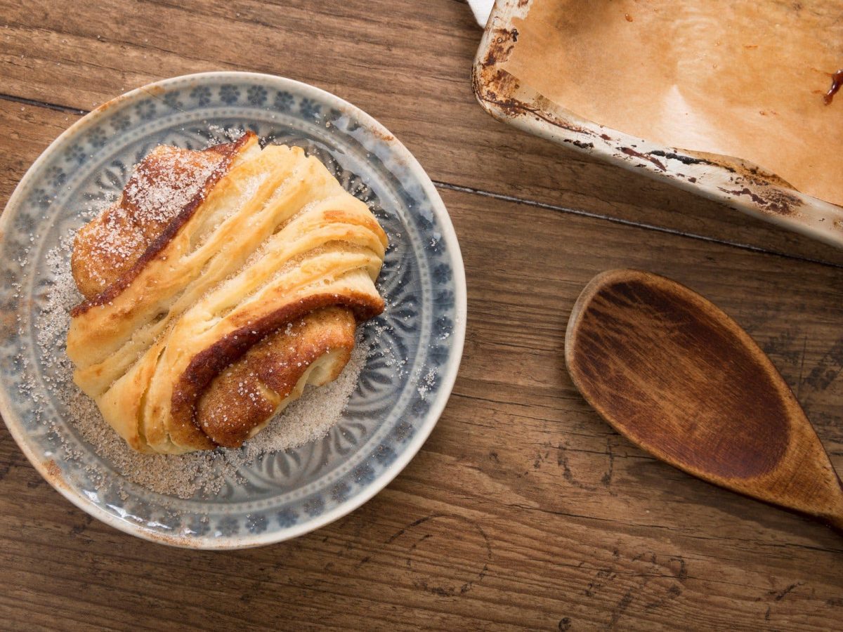 Franzbrötchen auf Teller, drapiert auf hölzernem Untergrund.