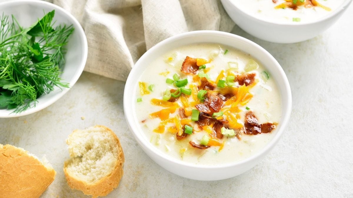 Kartoffelsuppe mit Speck, Käse und Frühlingszwiebeln in weißer Schale auf hellem Untergrund.