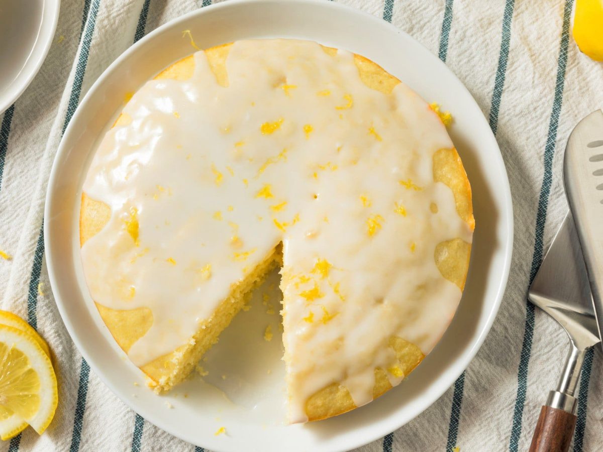 Limoncello-Kuchen mit Glasur auf gestreiftem Tischtuch.