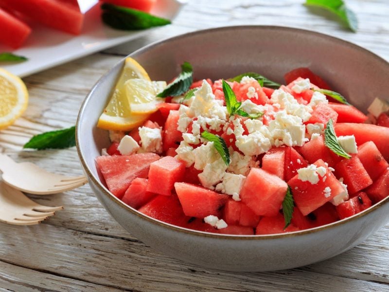 Eine Schale mit Wassermelone, Feta und Minze auf hölzernem Untergrund.