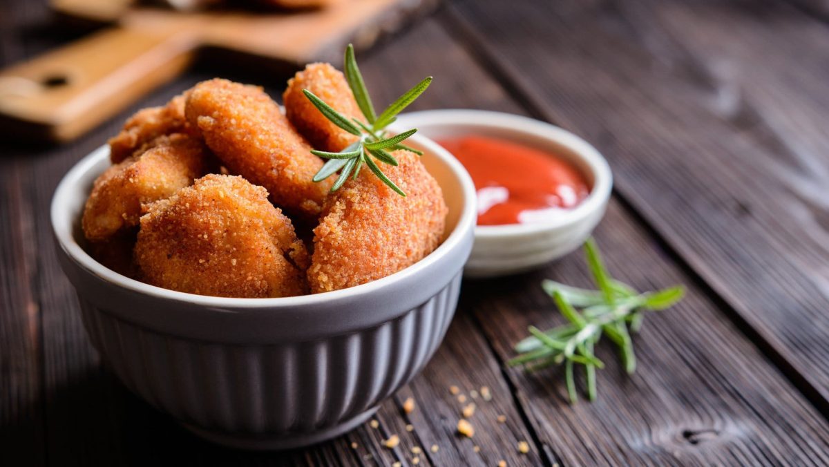 Mini-Schnitzel in weißer Schüssel auf dunklem Holz. Daneben steht ein Schälchen Ketchup.