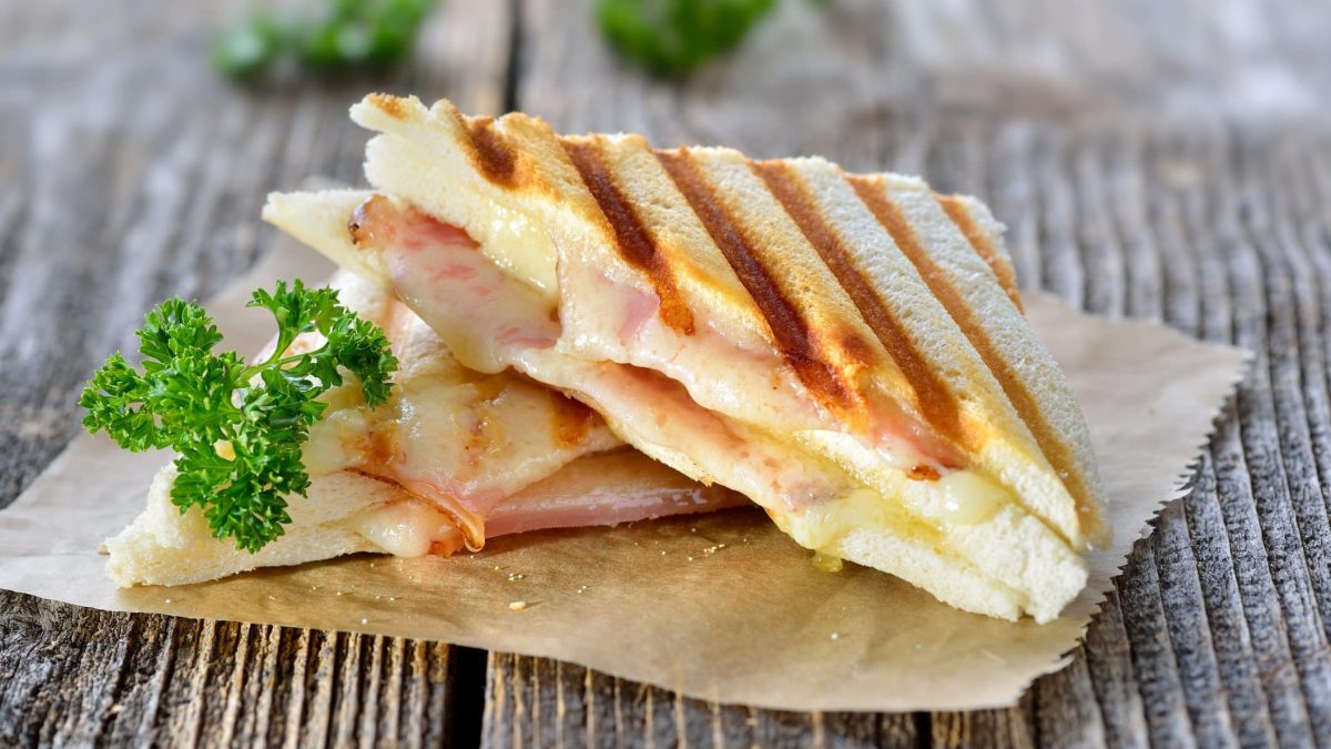 Italienische Panini mit Schinken und Käse auf Brotpapier. Das Ganze liegt auf einem Holz-Untergrund.