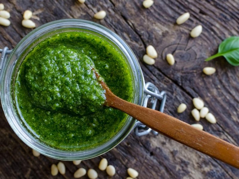 Pesto genovese mit Pinienkernen und Basilikum auf Holzuntergrund.