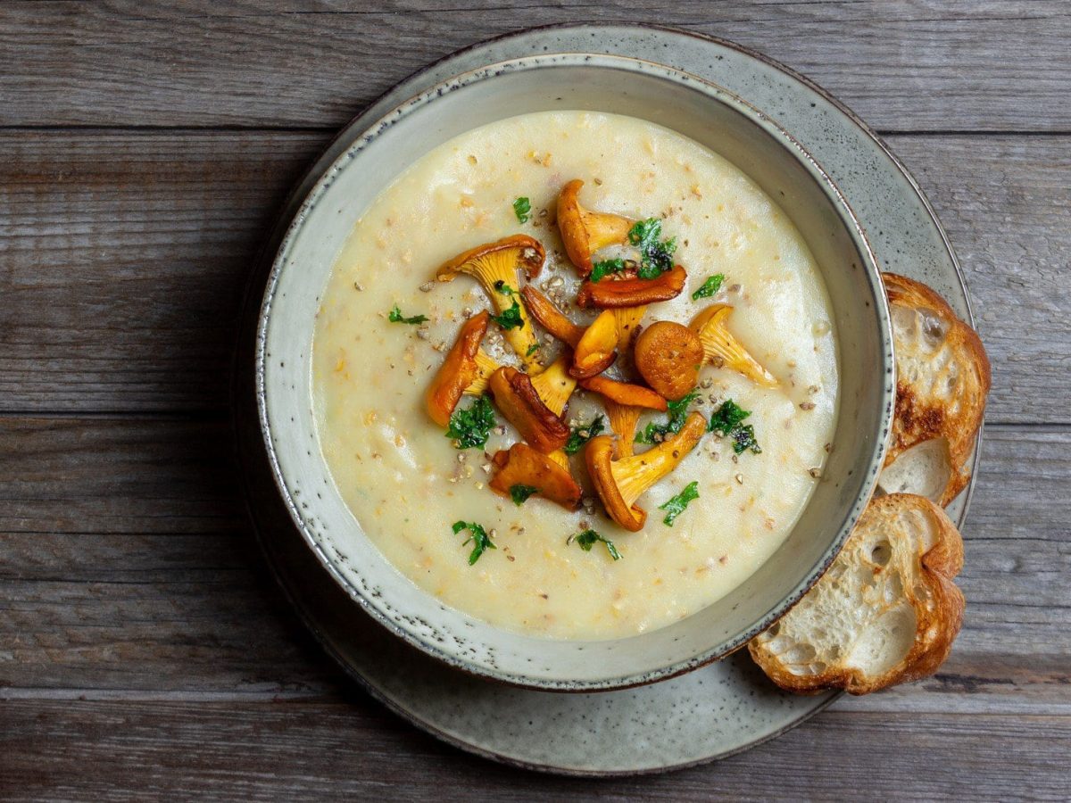 Pfifferling-Cremesuppe mit gebratenen Pfifferlingen auf hölzernem Untergrund.