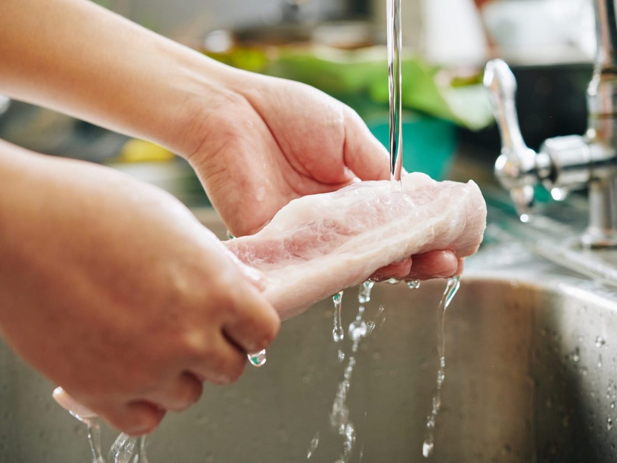 Rohes Fleisch wird unter Wasserhahn abgewaschen.