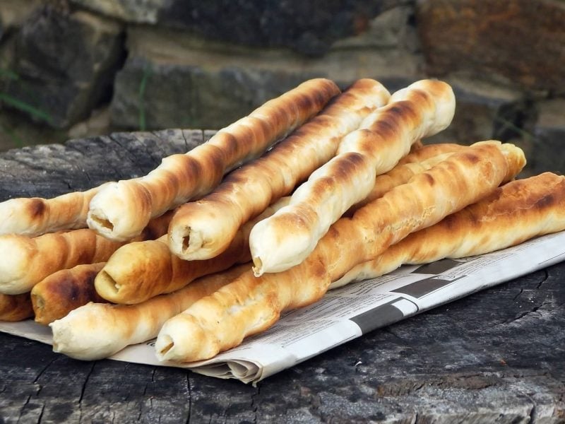 Einfaches über dem Feuer gebackenes Stockbrot, aufeinander geschichtet serviert auf einer Zeitung auf einem Holzblock.