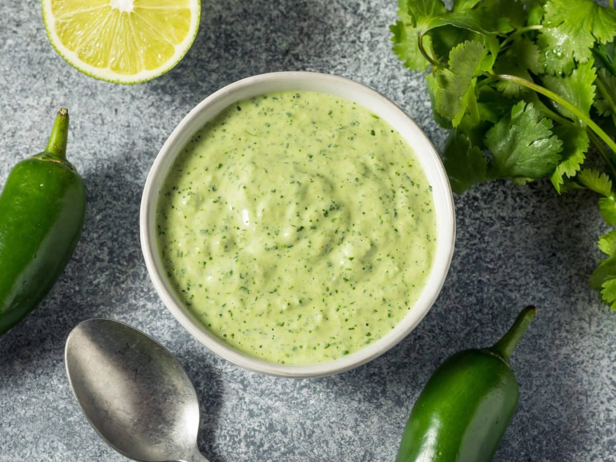 Grüne Aji-Sauce aus Peru in einem Gefäß neben grüner Chili, Limette und Koriander