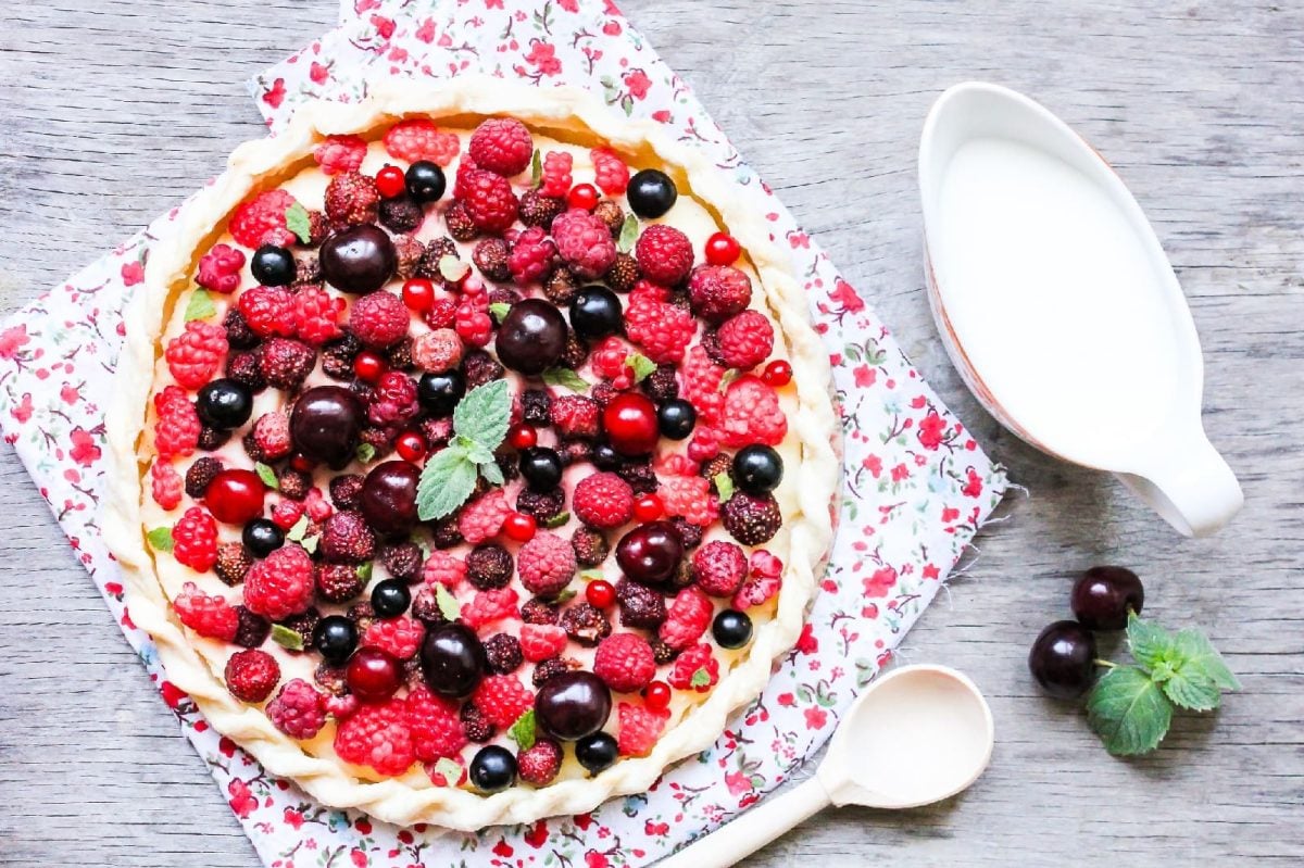 Beeren-Tarte auf einem bunten Küchentuch neben einer Kanne Milch