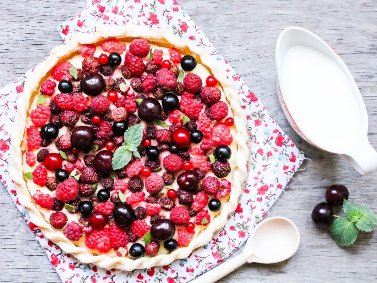 Beeren-Tarte auf einem bunten Küchentuch neben einer Kanne Milch