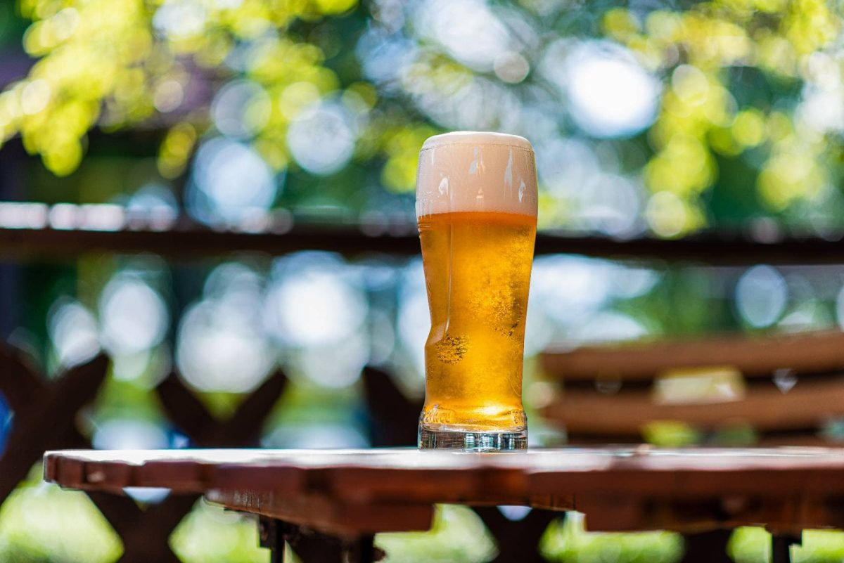 Biergärten Berlin: ein volles Bierglas auf einem Holztisch vor grünen Bäumen.
