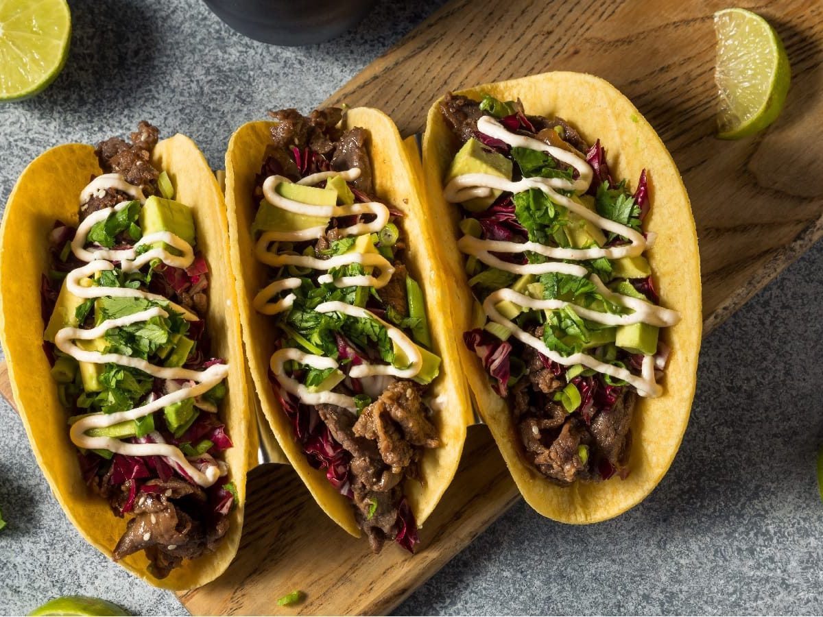 Bulgogi Tacos auf einem braunen Brett neben frischen Limetten und Koriander