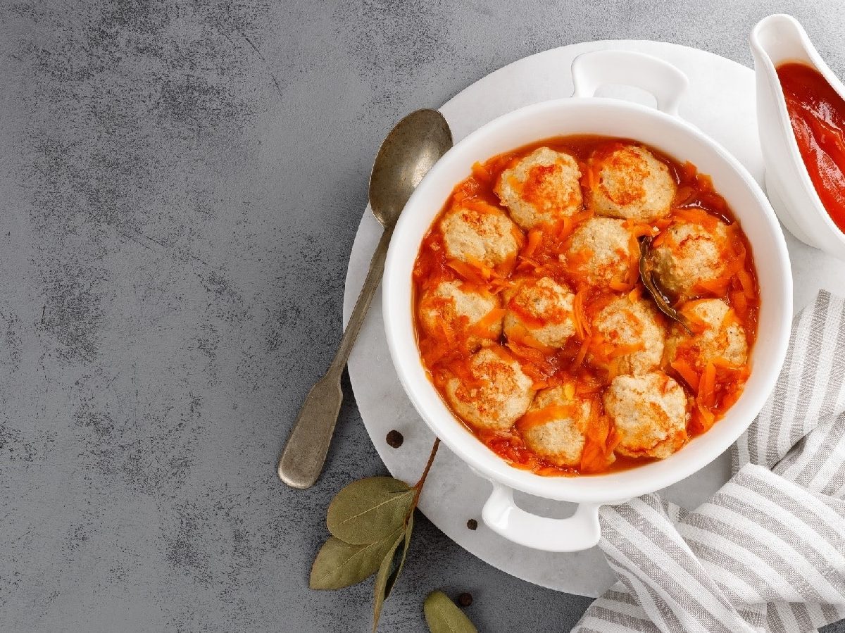 Fischfrikadellen in Tomatensauce auf einem gestreiften Küchentuch auf einem grauen Betontisch