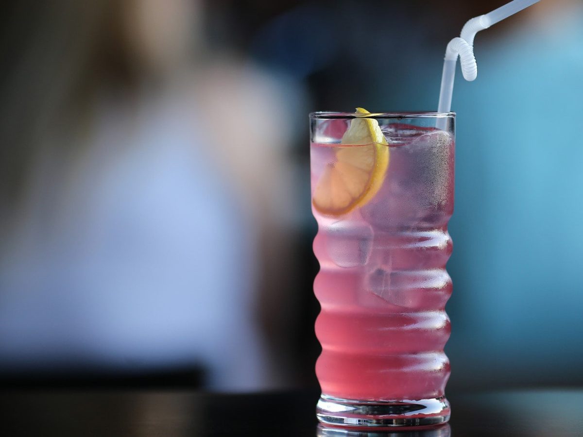 Gin Rosé Gin Cocktail mit Rosé Wein in besonderem Longdrink-Glas auf schwarzem Untergrund vor Bargästen.