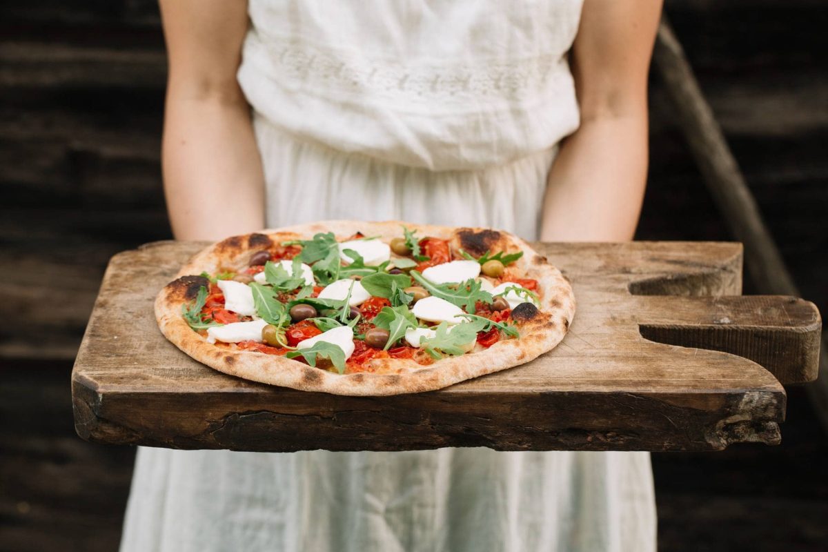 Italian Market Berlin: Eine Frau hält ein rustikales Holzbrett mit einer selbst gebackenen Pizza.