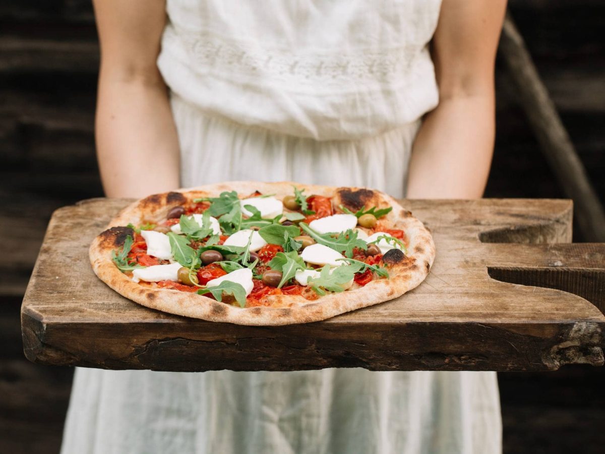 Italian Market Berlin: Eine Frau hält ein rustikales Holzbrett mit einer selbst gebackenen Pizza.