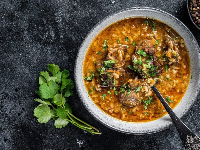 Eine georgische Lammsuppe steht auf einem Tisch. Die Lammsuppe heißt Karcho. Neben der Suppe liegen mehrere Stängel Koriander.