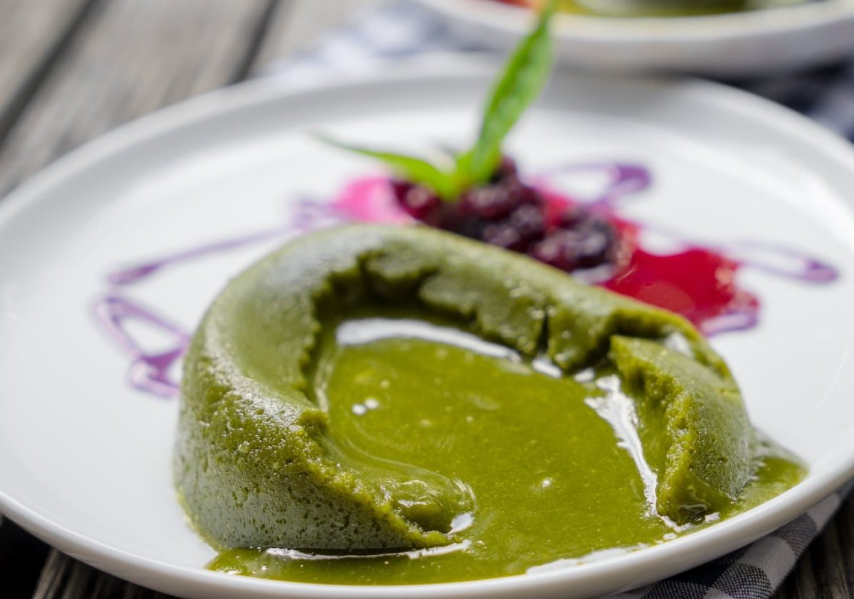 Ein zerlaufender Matcha Lava Cake auf einem weißen Telle r mit etwas Beerenragout.