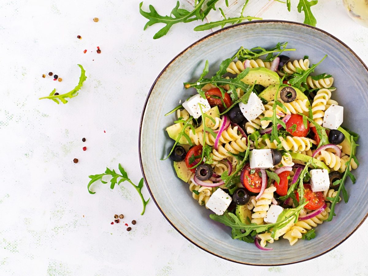 Nudelsalat mit Feta und Oliven in einer blaugrauen Schüssel.