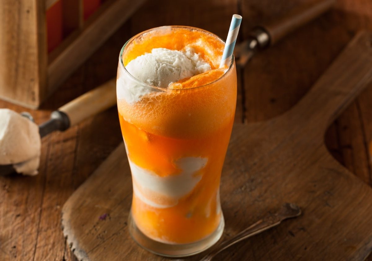 Ein großes Glas mit orange-weißer Schichtung der verschiedenen Orange Cream Float Zutaten. Alles auf einem dunklen Holztisch.