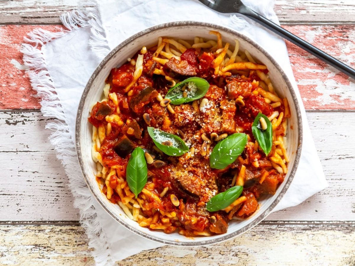 Ein Teller Pasta mit veganer Frischkäsesauce und frischem Basilikum in der Draufsicht, daneben eine Gabel.