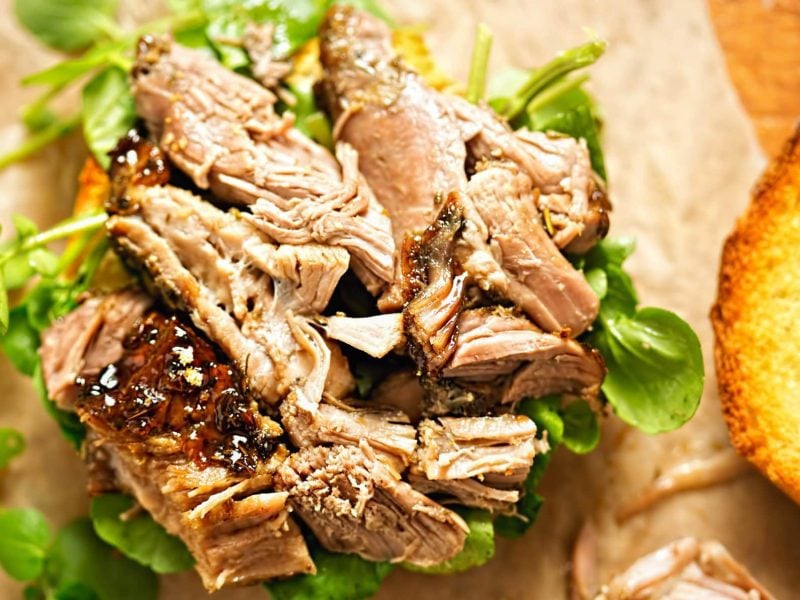 Tükisches Pulled Lamb Denizli Kebap auf Salatbett und hellem Untergrund. Daneben geröstetes Brot. Aufnahme aus der Vogelperspektive.