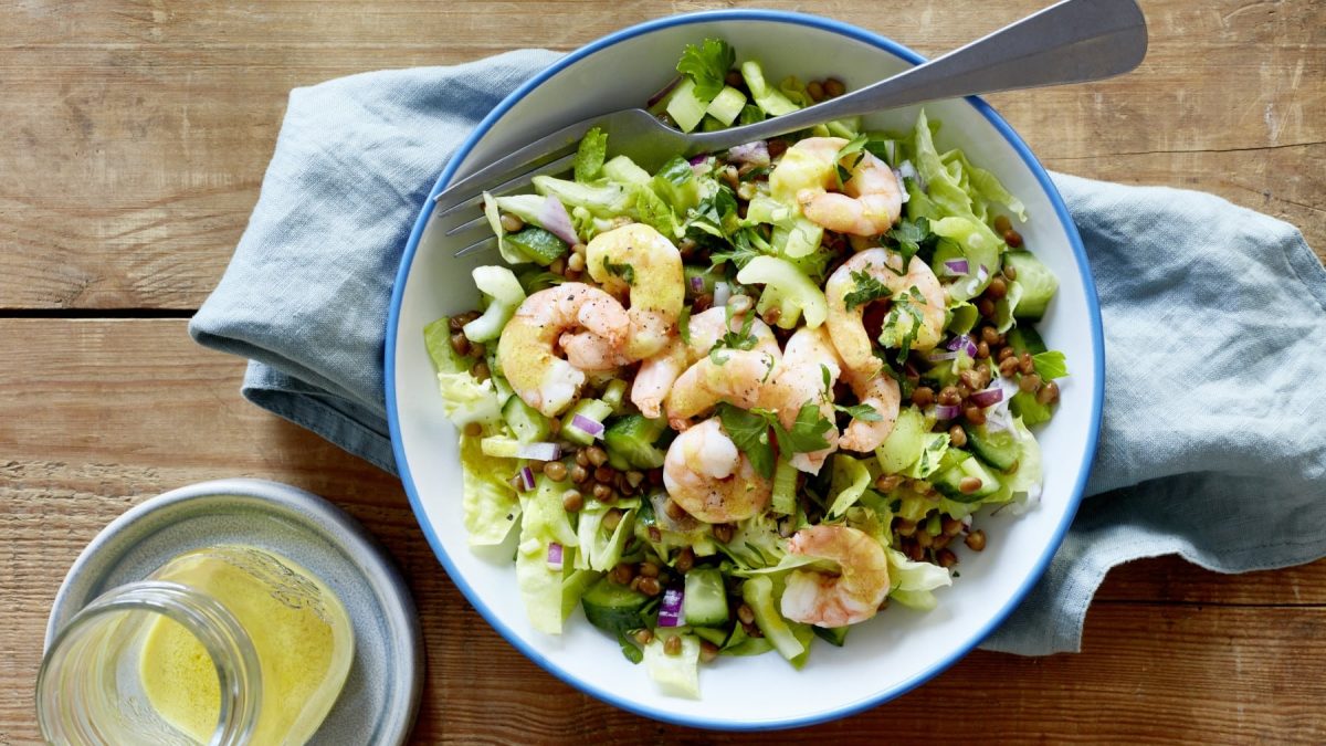 Eine weiße Schüssel mit blauen Rand in der sich Salat mit Linsen und Garnelen befindet.