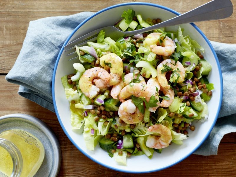 Eine weiße Schüssel mit blauen Rand in der sich Salat mit Linsen und Garnelen befindet.