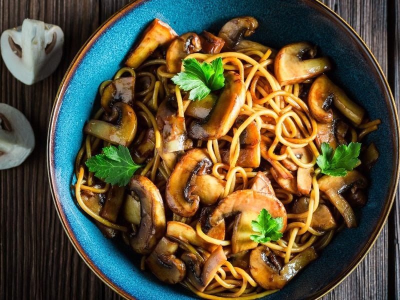 Spaghetti mit Sojabutter und Pilzen in einer blauen Schüssel auf einem Holztisch