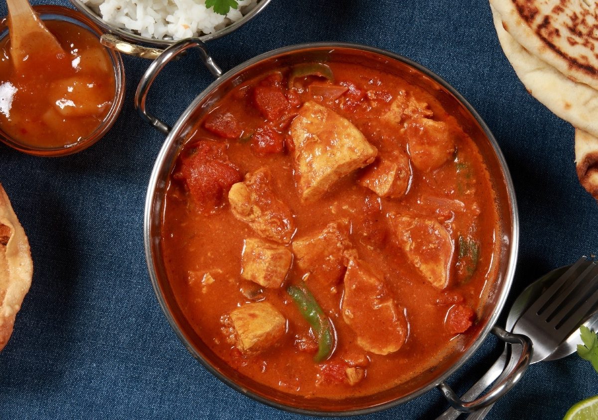 Eine Schale Tandoori Masala auf dunkelblauem Untergrund mit Naan an der Seite.