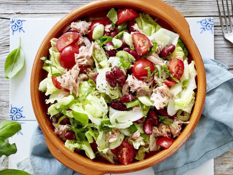 Eine Schüssel Thunfisch-Salat mit Kidneybohnen auf einem blauen Küchentuch neben einer Gabel