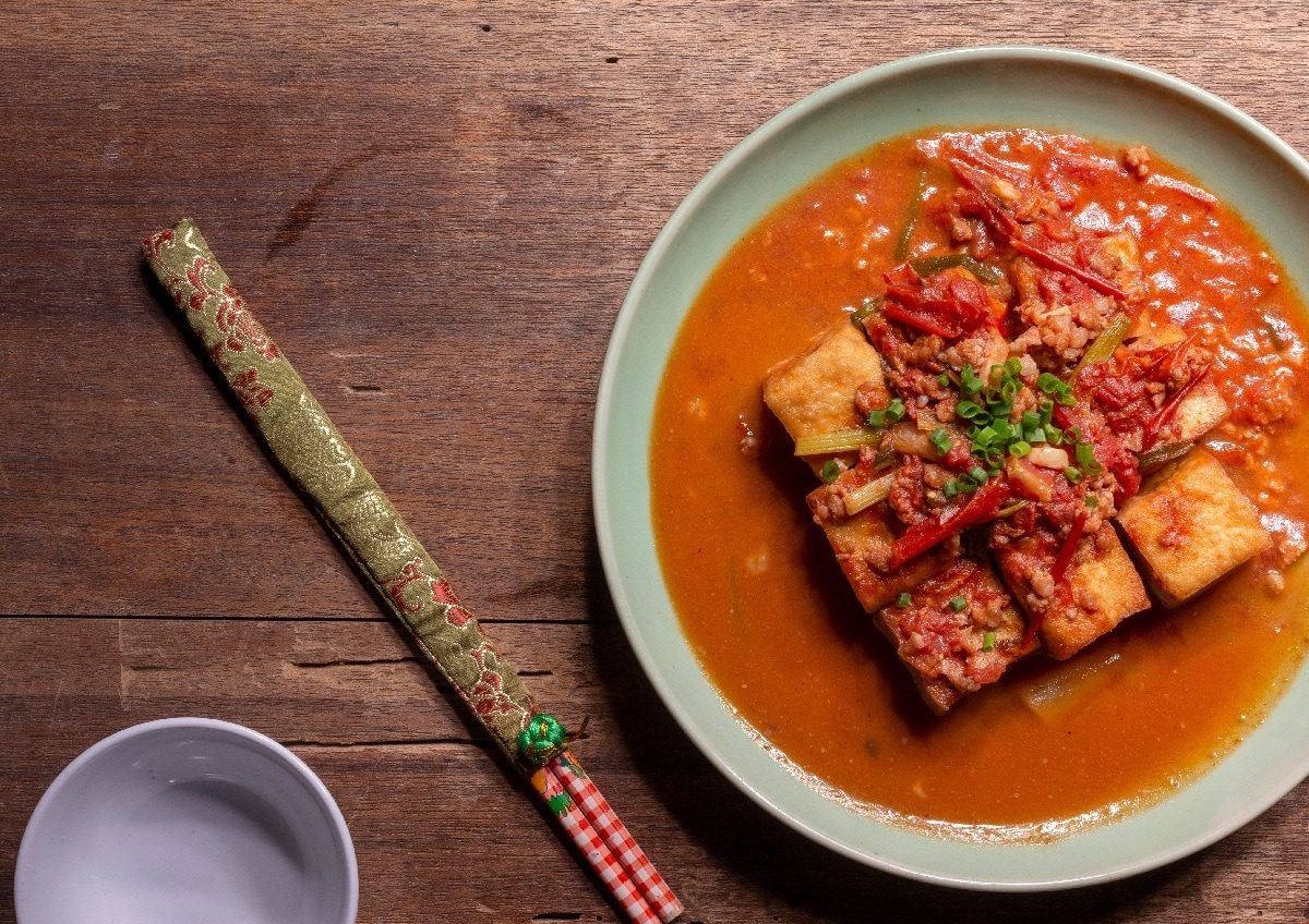 Eine Schüssel Tofu in Tomatensauce neben einem Paar Stäbcgen