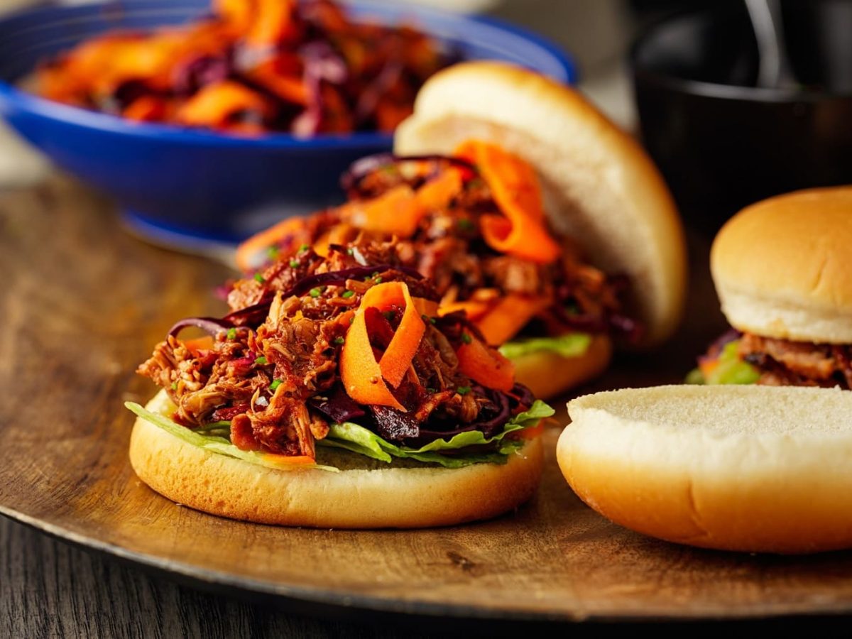 Drei vegane Jackfruit-Burger mit Coleslaw auf einem runden Brett.