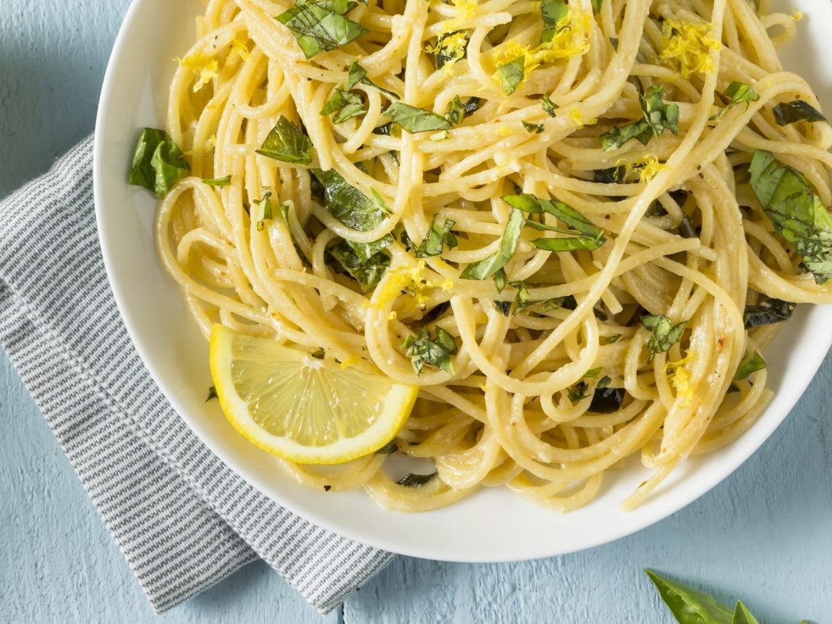 Ein Teller vegane Zitronen-Knoblauch-Pasta mit Zitronenscheiben und gehacktem Basilikum in der Draufsicht.