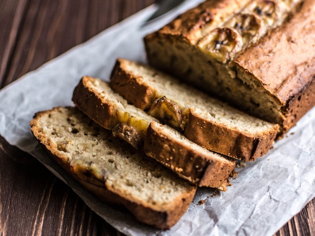 Ein angeschnittenes veganes Bananenbrot mit Bananenscheiben obendrauf.