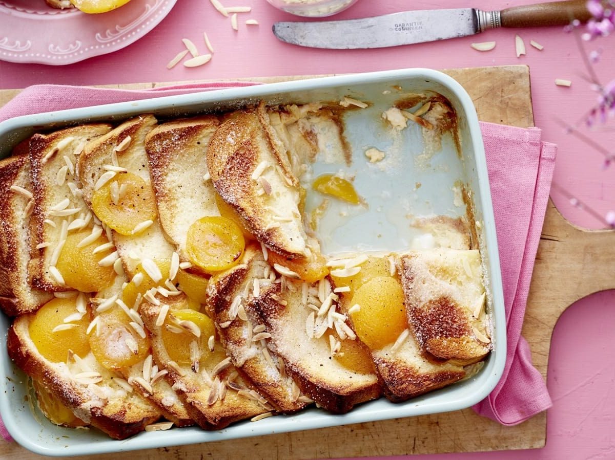 In einer Auflaufform liegt eine Portion Brioche-Aprikosen-Auflauf. Er ist mit Mandelnsplittern und Aprikosen verziert.