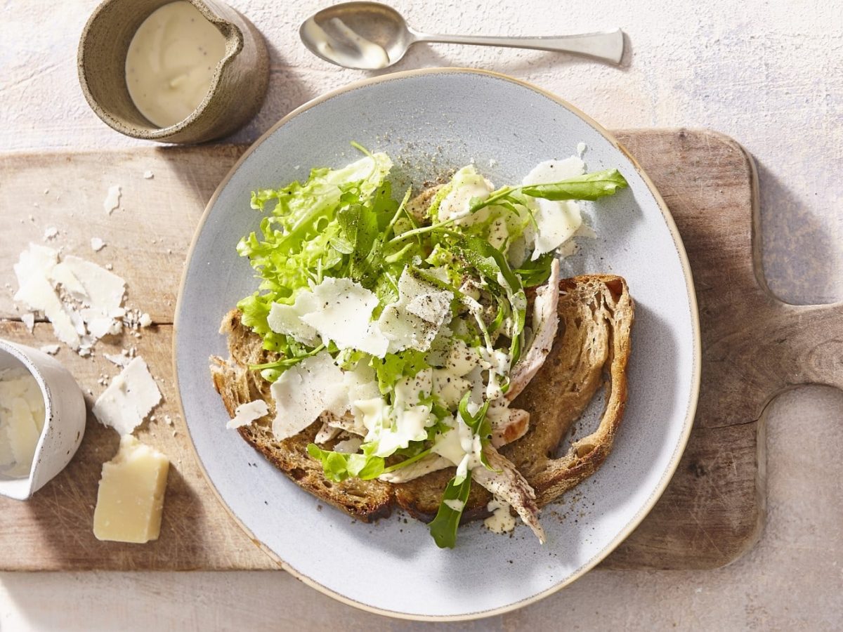 Grünes Caesar-Salat-Sandwich mit Parmesan, Geflügelbrust, Salat und selbstgemachtem Dressing auf rustikalen Bauernbrot, serviert auf einem weißen Teller auf einem Holzbrett.